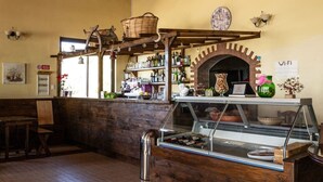 Interior rústico com balcão de madeira, prateleiras com garrafas, forno de tijolos e sinal de Wi-Fi.
