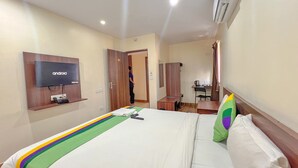 A hotel room with a bed, a TV mounted on the wall, a desk with a chair, and an air conditioning unit. - The Prime Hotel HBR (Bengaluru)
