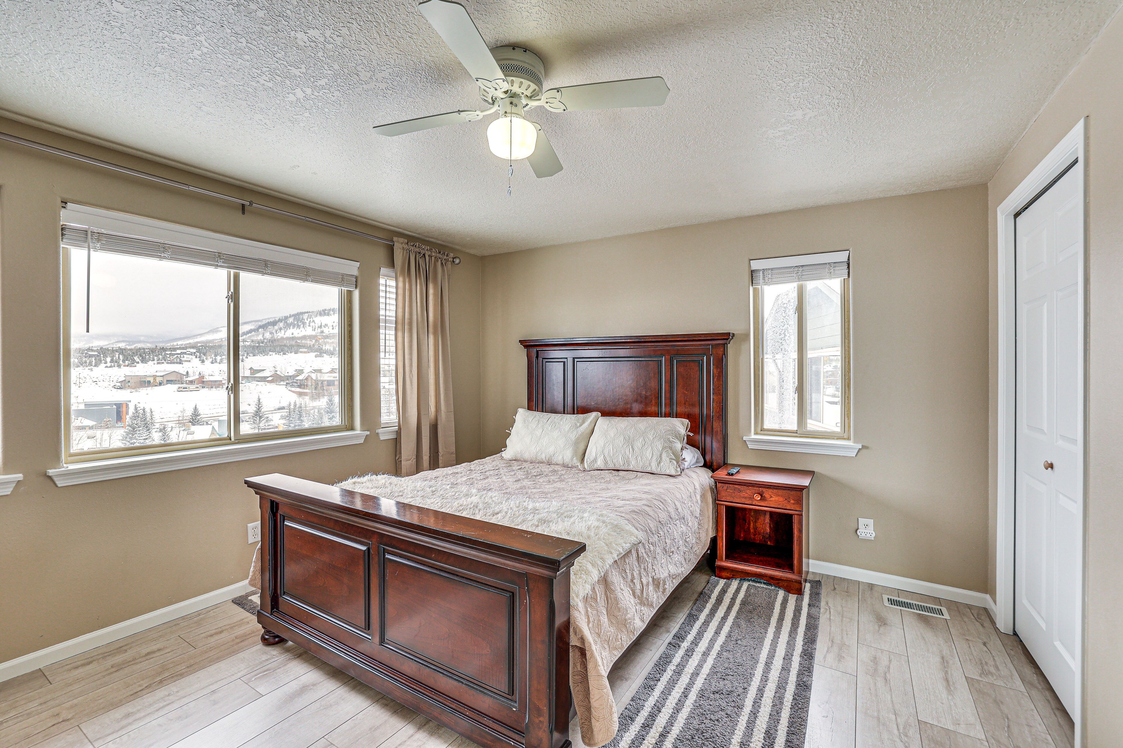 A bedroom with a wooden bed, two bedside tables, a ceiling fan, and large windows with curtains.