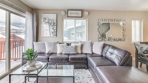 A living room with a leather sofa, a glass coffee table, and a view of a snowy landscape through large windows. - 5 Mi to Keystone Resort: Mountain-View Townhome! (Dillon)