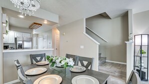 A dining area with a wooden table set for four, a chandelier, and a view of the kitchen and stairs in the background. - 5 Mi to Keystone Resort: Mountain-View Townhome! (Dillon)
