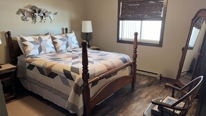 A bedroom with a wooden four-poster bed, a bedside table with a lamp, a chair, and a window with blinds. - Quiet place on the prairie near Wessington, SD.  (Wessington)