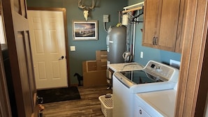A laundry room with a washing machine, dryer, and a large water heater. There is a door leading to another room and a wall-mounted picture. - Quiet place on the prairie near Wessington, SD.  (Wessington)