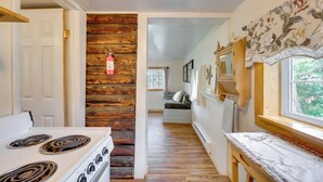 A kitchen with a wooden accent wall, a stove, and a window with a view of greenery. - 'Minnehaha' Allenspark Cabin Near Hiking! (Allenspark)