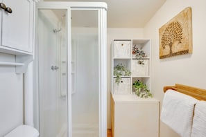 Ein Badezimmer mit Duschkabine aus Glas, einer weißen Toilette, einem hölzernen Kopfteil und einem Regal mit Dekoration.