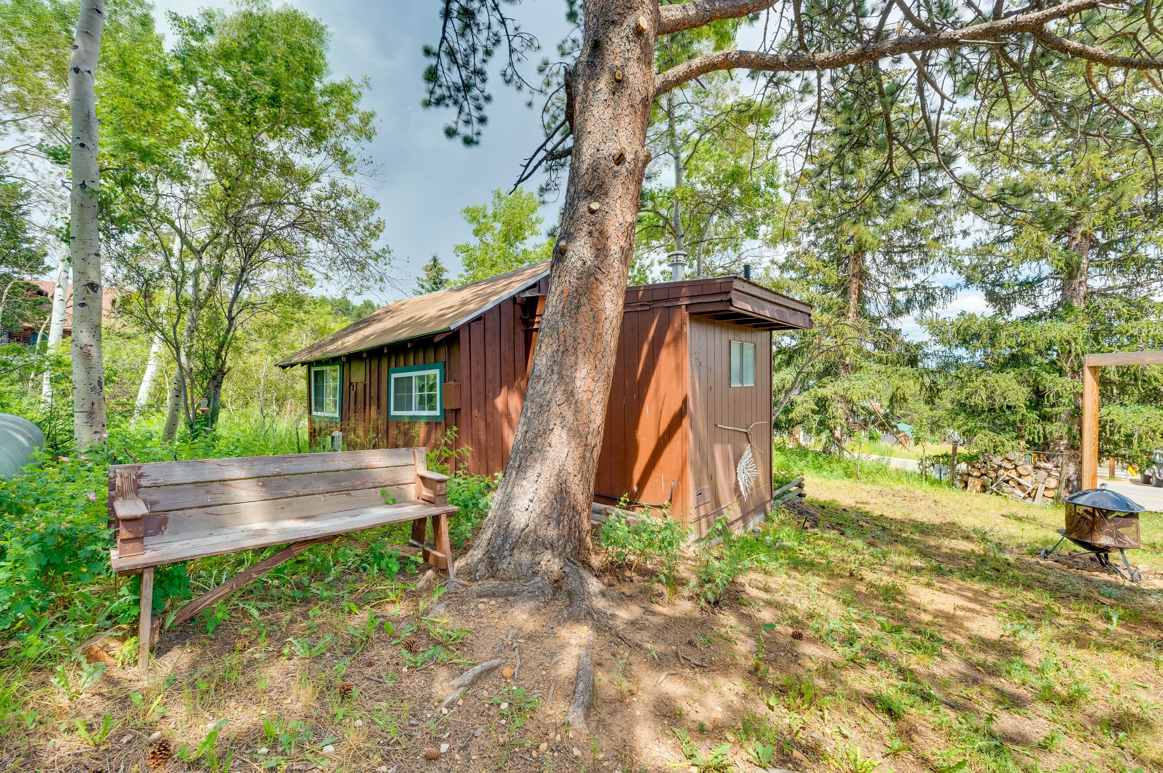 Une cabane en bois rustique, avec un banc et un barbecue, située dans une zone boisée.
