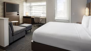 A hotel room with a large bed, a desk with a chair, a TV mounted on the wall, and a window with a city view.