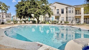 A swimming pool surrounded by lounge chairs and a building with multiple balconies.
