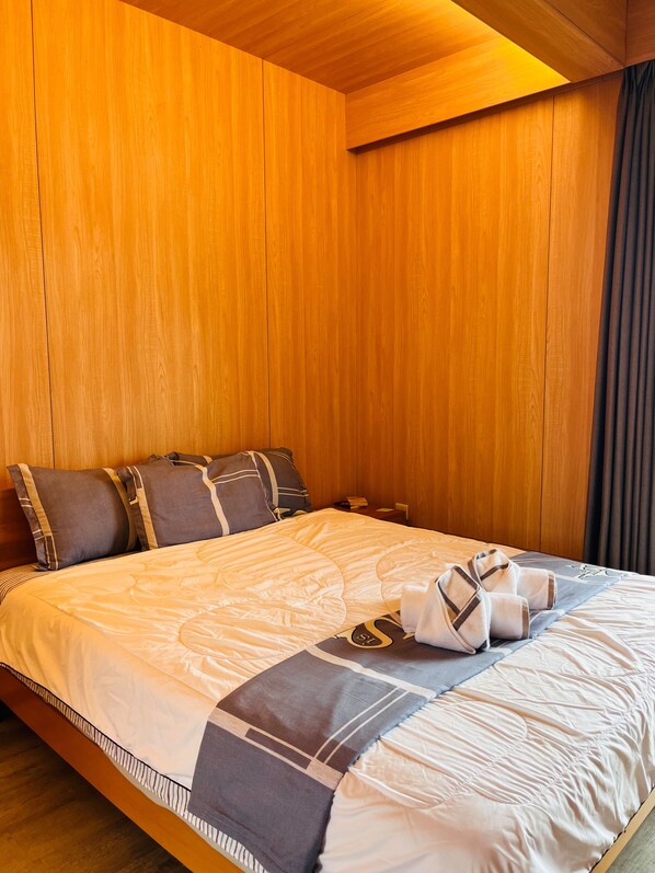 A hotel room with a wooden panel wall, a neatly made bed with pillows and a blanket, and a dark curtain on the window. - Calypso Hotel Nevis (Camps)