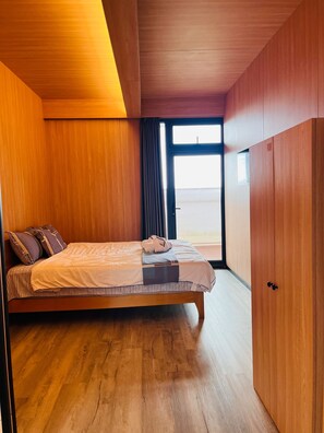 A modern bedroom with a wooden bed, a view through a window, and a wardrobe. - Calypso Hotel Nevis (Camps)