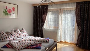 Ein Schlafzimmer mit einem Bett, Kissen, einer Pendelleuchte, einem Fenster mit Vorhängen und einem Bild an der Wand.