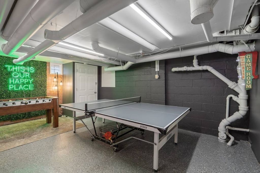 A ping pong table in a room with a neon sign, a foosball table, and a sign indicating a game room.