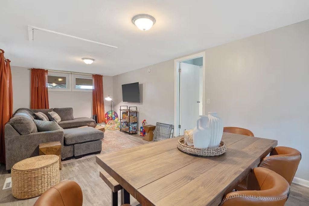 Una sala de estar con sofá, reposapiés y una mesa de comedor de madera con sillas.