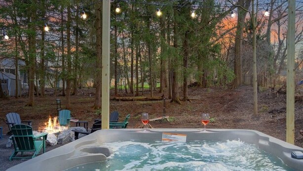 A hot tub with a fire pit and chairs, surrounded by trees and a sunset in the background. - Hot Tub, Game Room, Near SU, sleeps 10 (Syracuse)