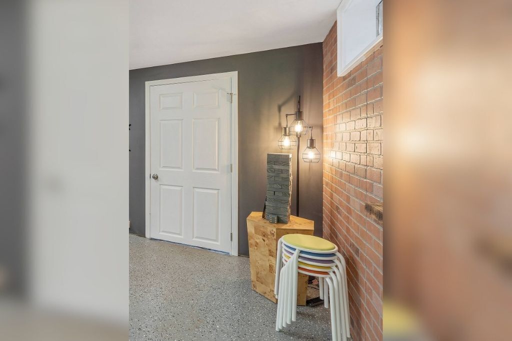 A hallway with a white door, a brick wall, and a small table with stacked chairs.