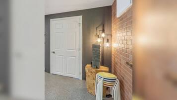 A hallway with a white door, a brick wall, and a small table with stacked chairs.