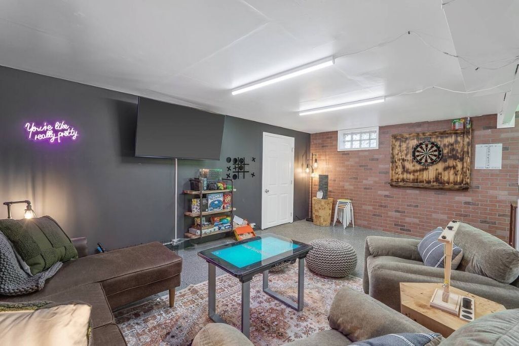 A modern living room with a dartboard, a neon sign, and a bookshelf.