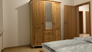 Un dormitorio con un armario de madera, una cama con ropa de cama estampada y una puerta que da a otra habitación.