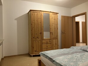 A bedroom with a wooden wardrobe, a bed with patterned bedding, and a door leading to another room. - Geräumige Ferienwohnung in Ruhiger Lage Nahe Ingolstadt (Hepberg)