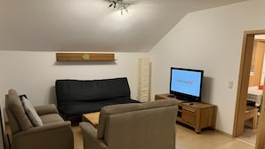 Una sala de estar moderna con un sofá, dos sillones, un mueble de televisión de madera y un televisor de pantalla plana mostrando “PREMIUM”.
