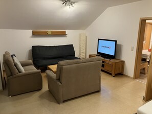A modern living room with a sofa, two armchairs, a wooden TV stand, and a flat-screen TV displaying "PREMIUM". - Geräumige Ferienwohnung in Ruhiger Lage Nahe Ingolstadt (Hepberg)