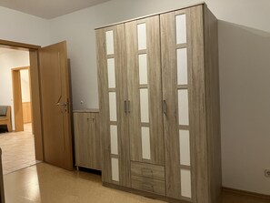 A wooden wardrobe with multiple compartments and a small drawer, located in a hallway with a tiled floor and a door leading to another room. - Geräumige Ferienwohnung in Ruhiger Lage Nahe Ingolstadt (Hepberg)