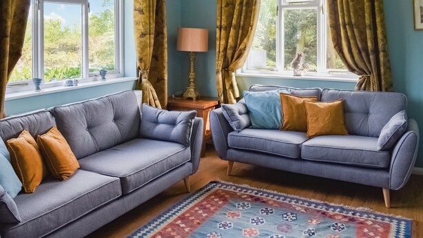 A room with two grey sofas, a patterned rug, and curtains. - 4 bedroom accommodation in Saxmundham (Saxmundham)