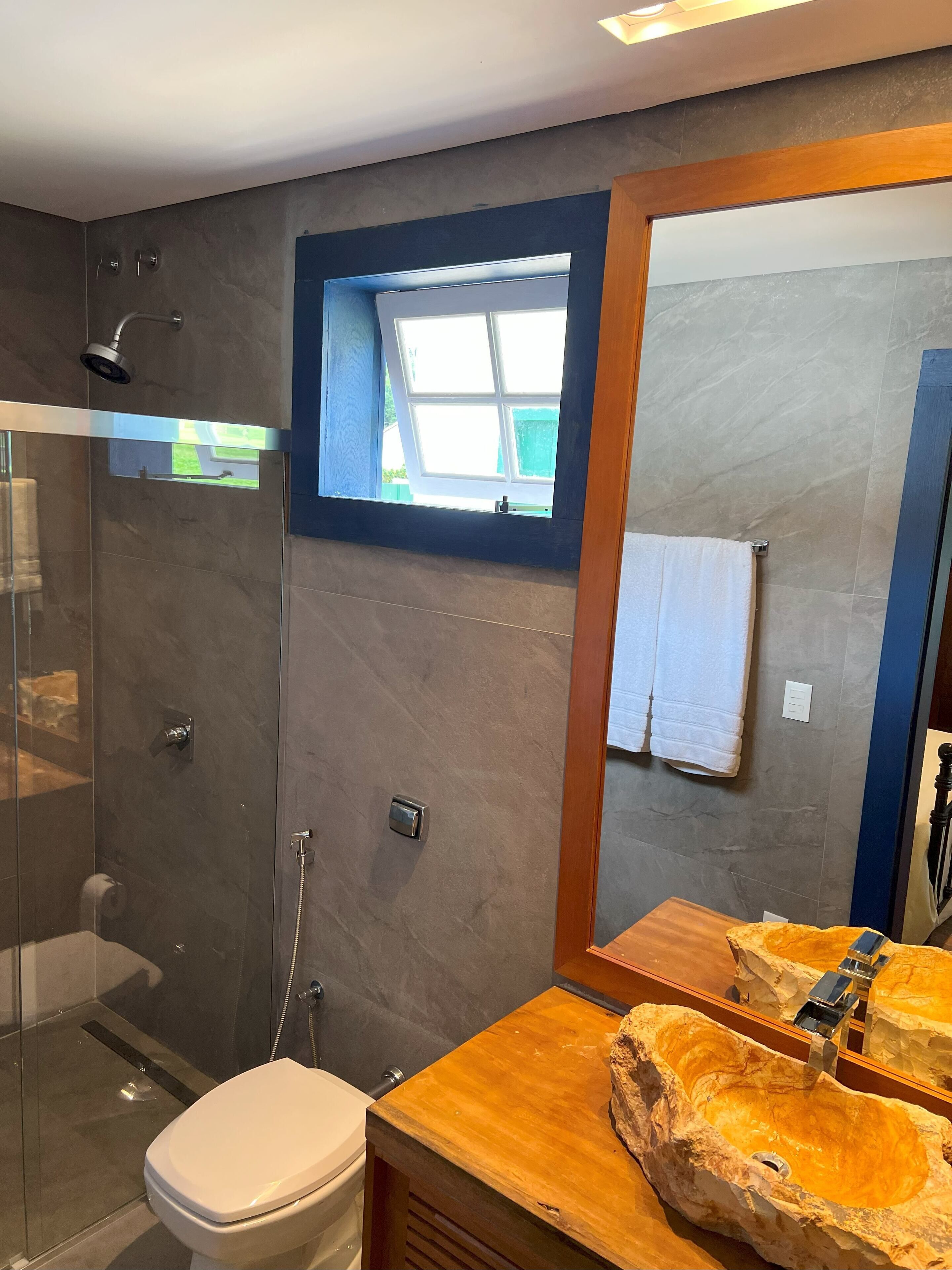A modern bathroom with a glass-enclosed shower, a wooden vanity with a unique sink, and a large mirror.