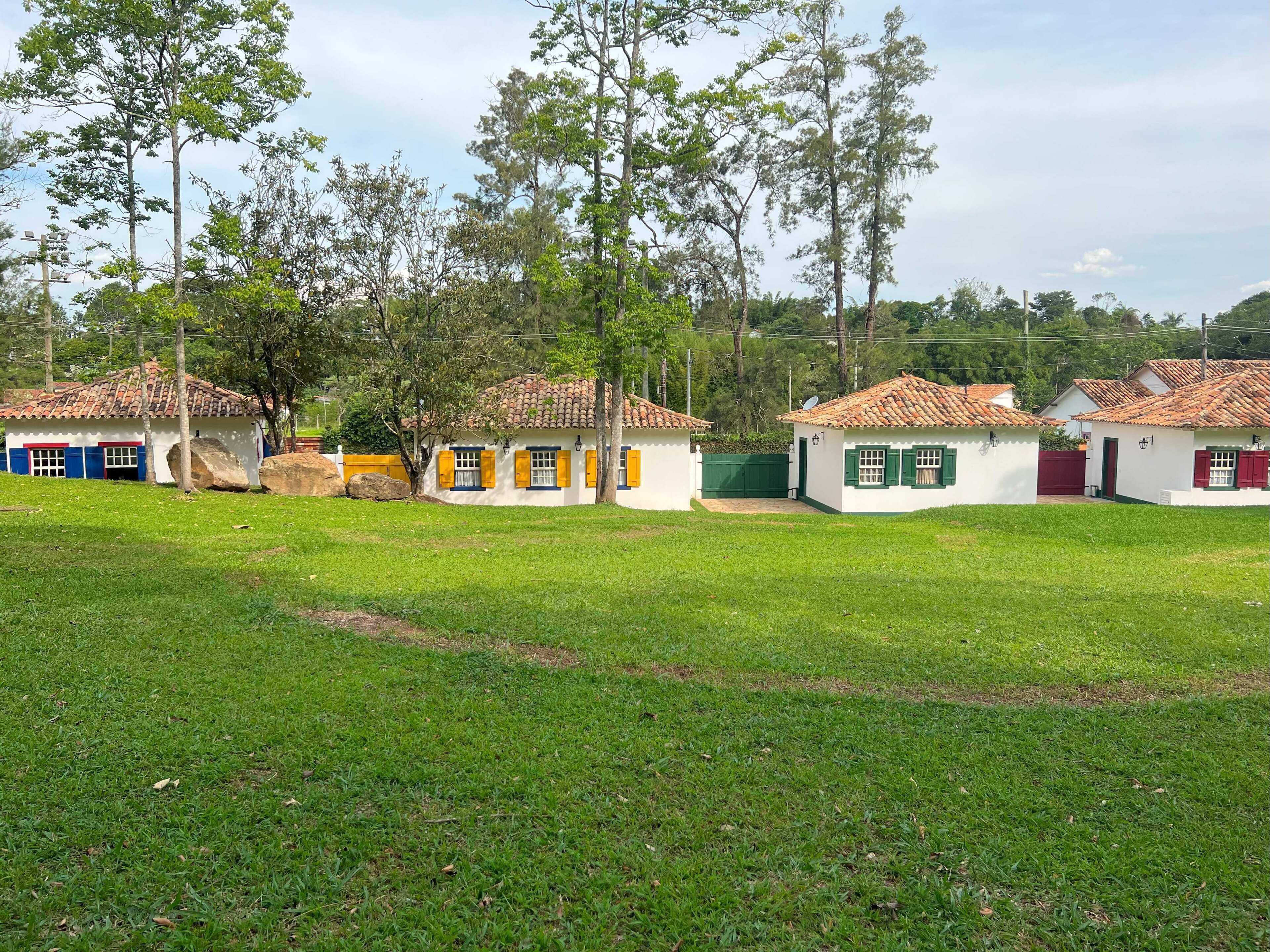 Una hilera de casas pequeñas, de color blanco, con tejados rojos y contraventanas verdes, rodeadas de césped y árboles.