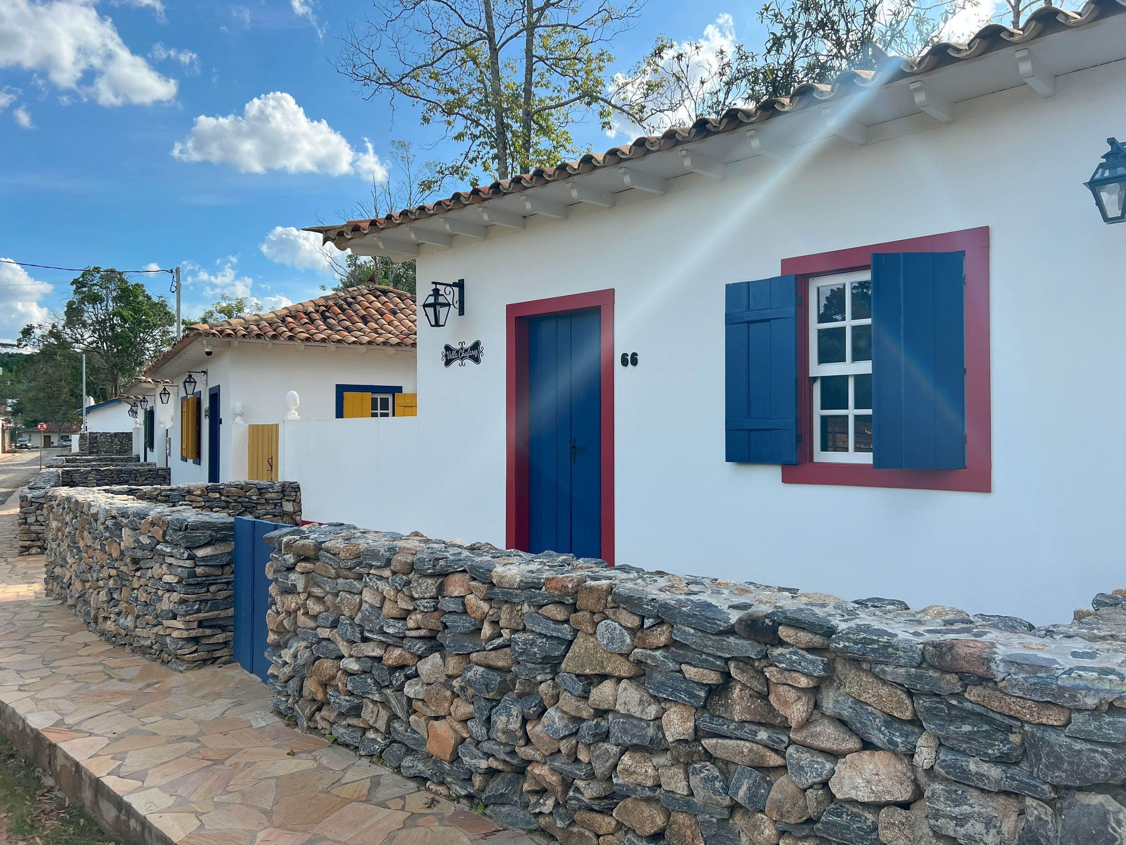 A white building with a stone wall, a blue door, and a blue window with shutters.