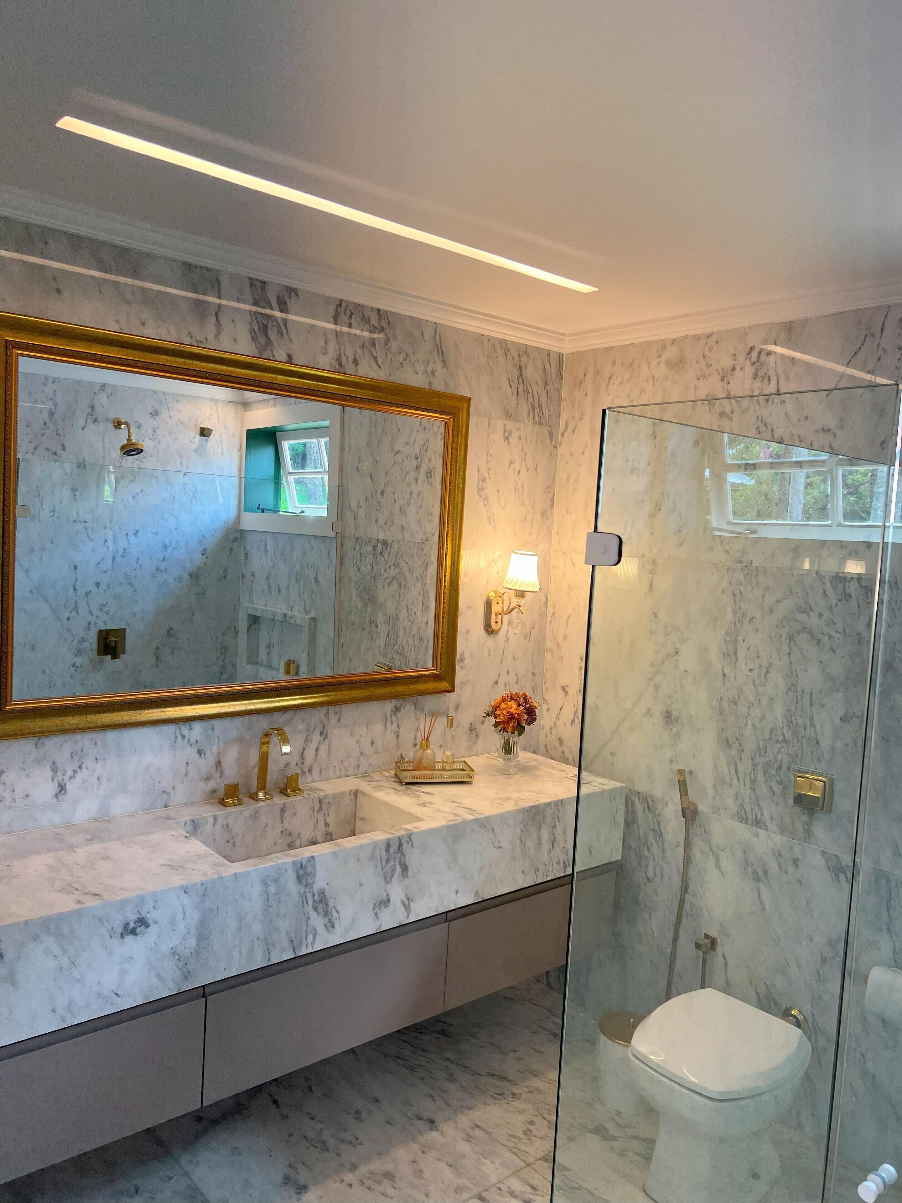 Une salle de bain avec un meuble-lavabo en marbre, un grand miroir avec un cadre doré, une cabine de douche en verre et des toilettes.