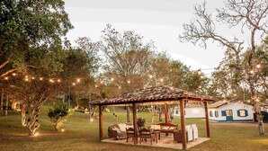 A gazebo with outdoor seating, surrounded by trees and a house in the background. - Villa Chafariz  (Tiradentes)