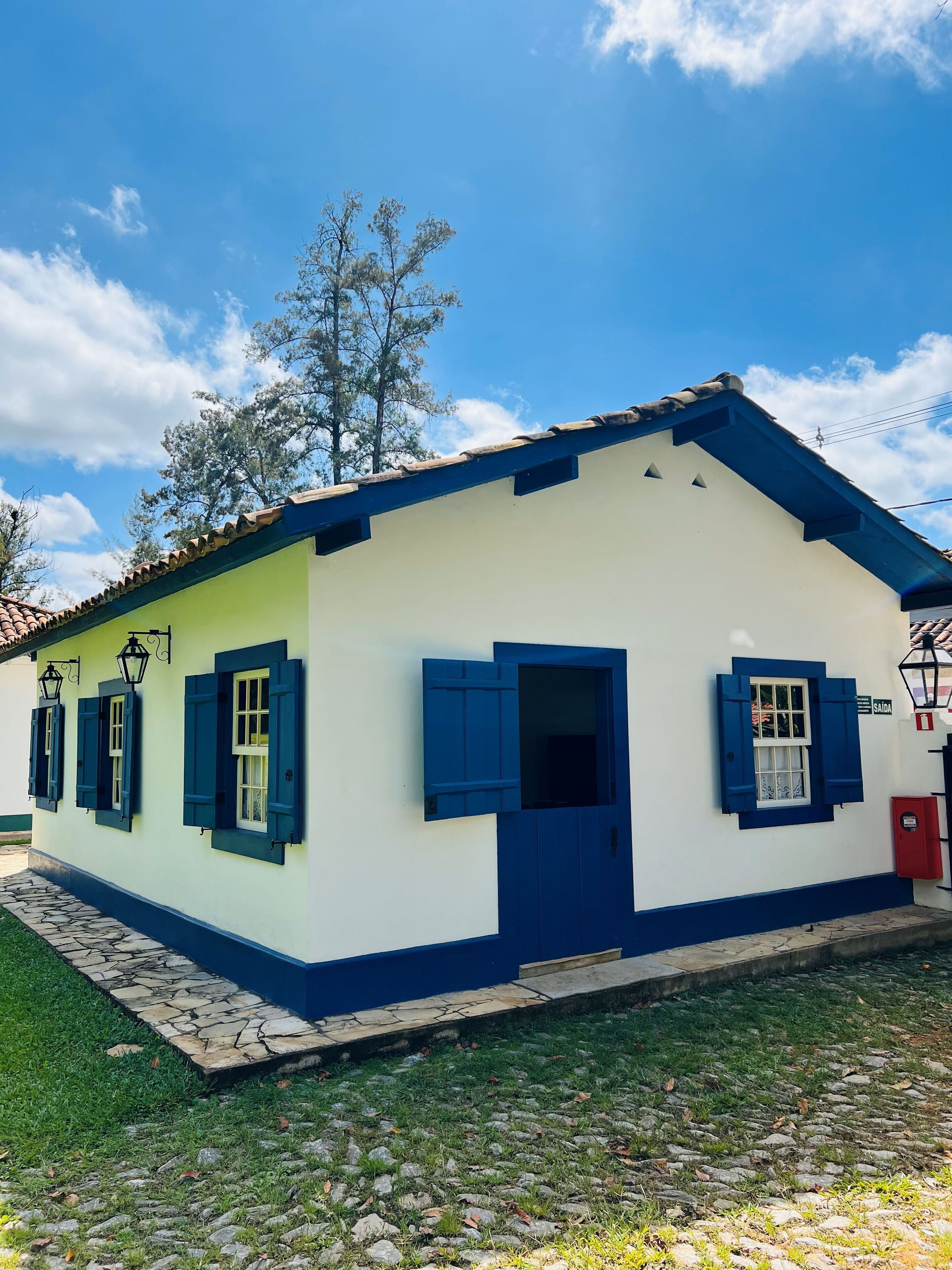 Edificio de una planta con fachada blanca y detalles azules, que presenta una puerta central y ventanas con contraventanas azules.