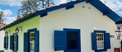 Edificio de una planta con fachada blanca y detalles azules, que presenta una puerta central y ventanas con contraventanas azules.
