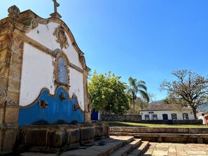 A historic building with a white facade and blue accents, featuring a central arched window and a stone staircase leading to a door.