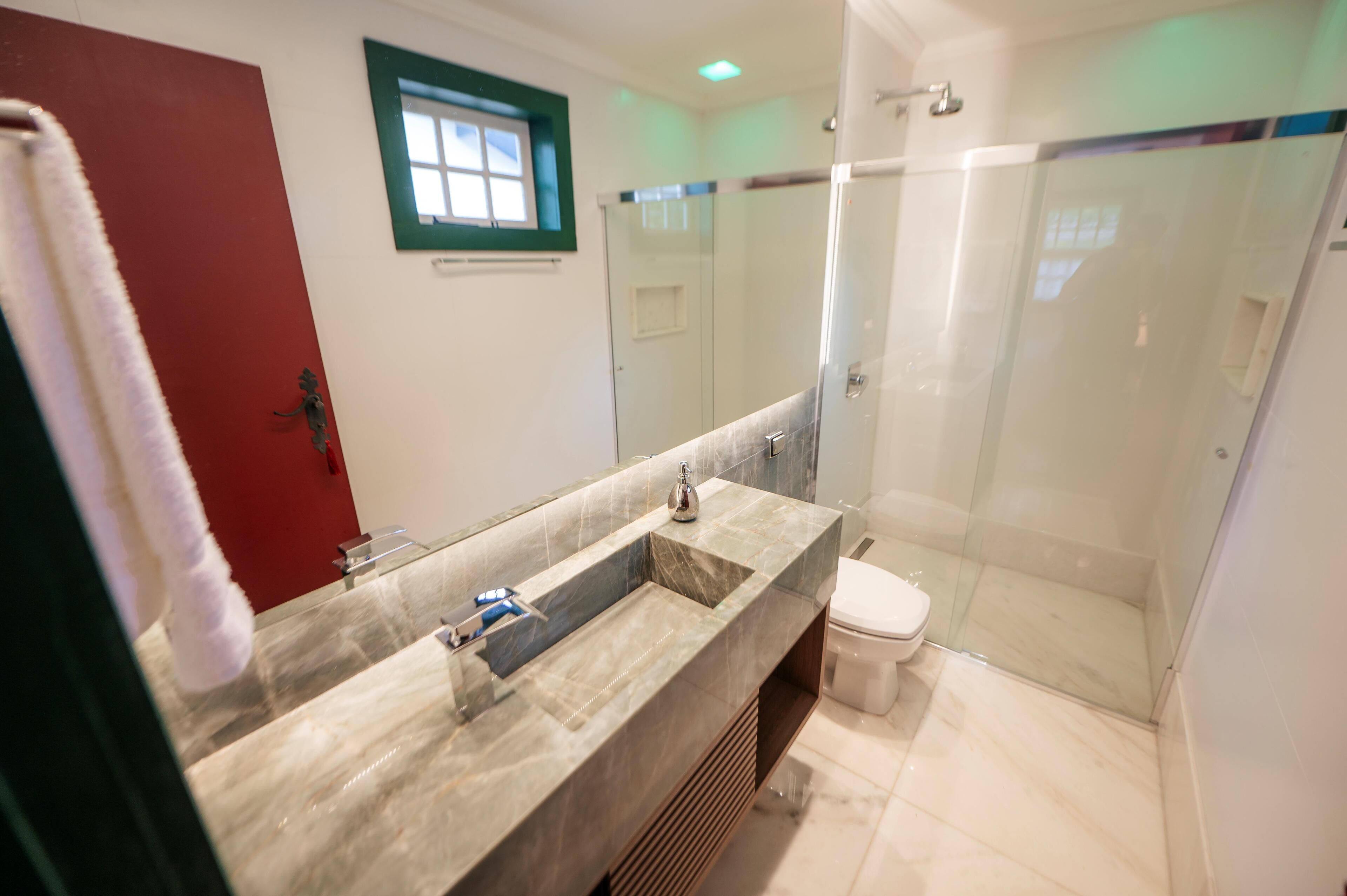 A bathroom with a marble sink, a glass shower enclosure, and a red door.