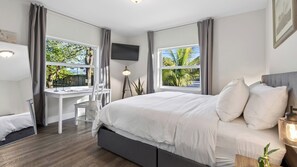 A modern hotel room with a large bed, a desk, and a TV. - Hot Tub, Firepit, Deck | 10mins to Beach | Middle Terrace Cottage by AvantStay (Fort Lauderdale)