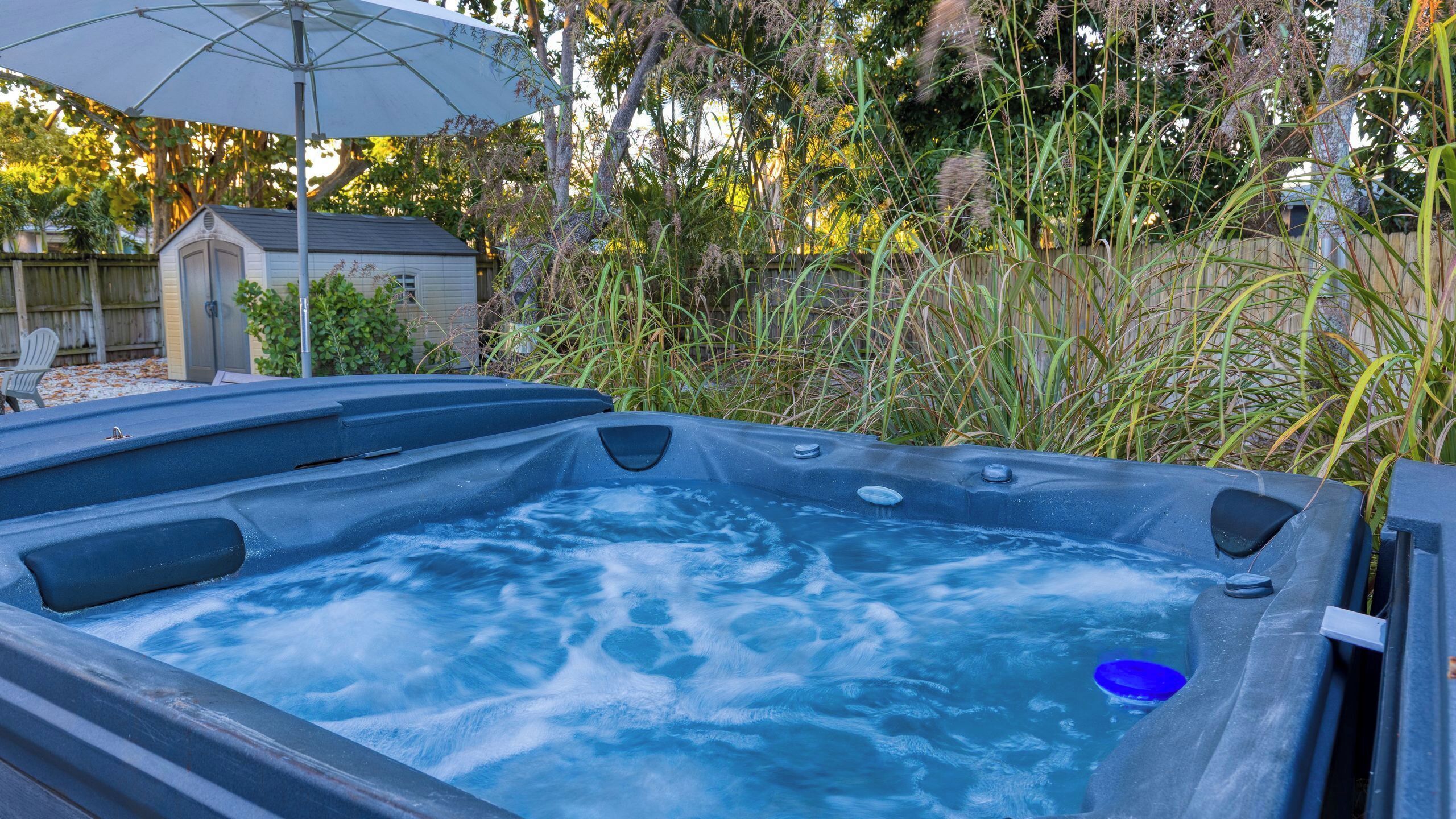 A hot tub with a blue cover, surrounded by a wooden fence and various plants.