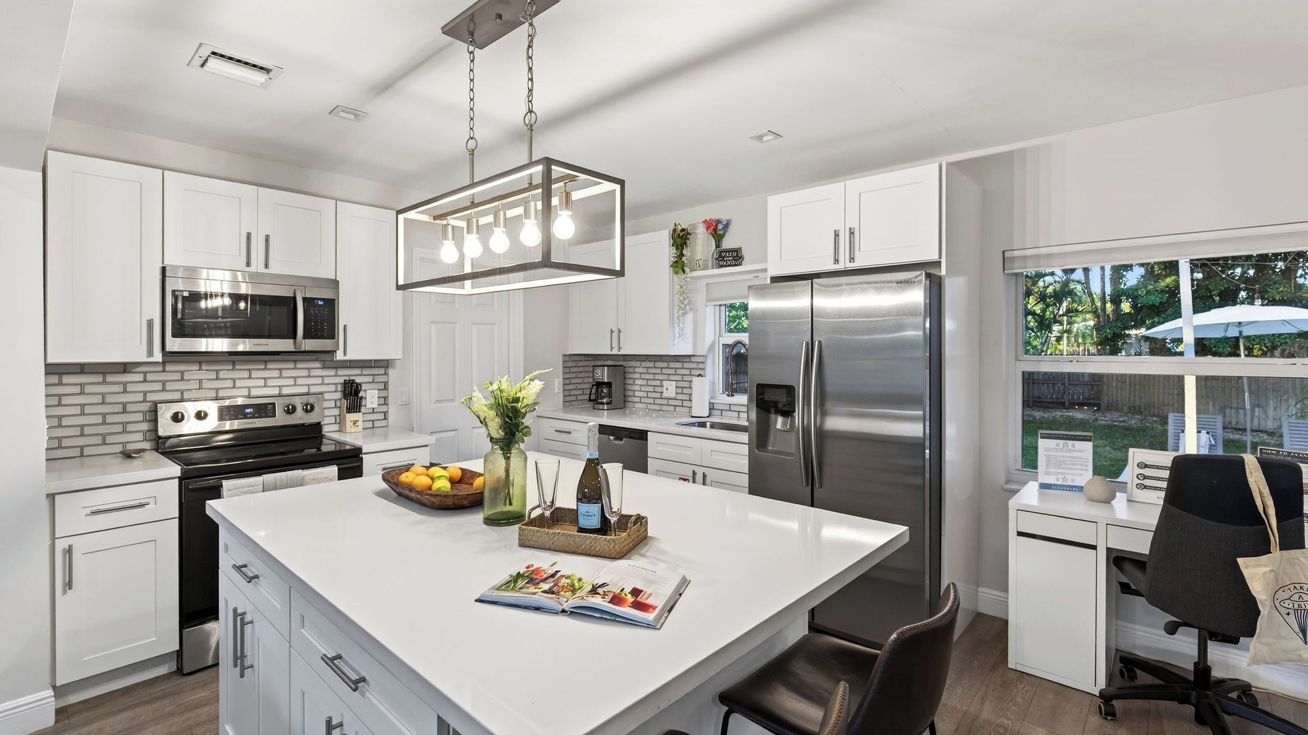 A modern kitchen with white cabinetry, stainless steel appliances, and a central island with a magazine and decorative items.