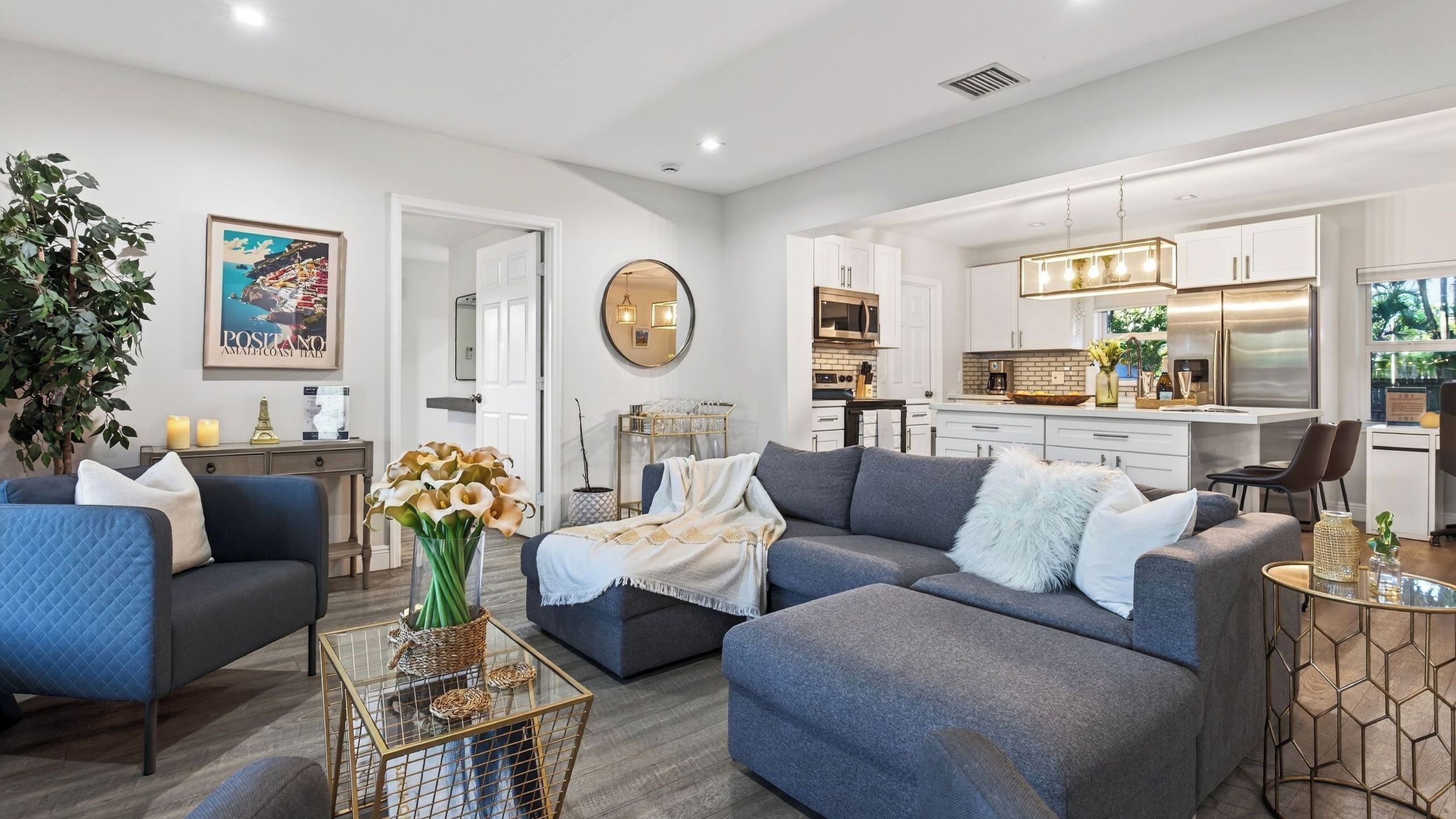 A modern living room with a grey sofa, a coffee table, and a dining area with a kitchen in the background.
