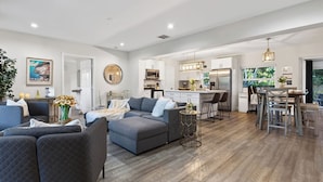 A spacious living area with a grey sofa, a coffee table, and a dining area with bar stools. - Hot Tub, Firepit, Deck | 10mins to Beach | Middle Terrace Cottage by AvantStay (Fort Lauderdale)