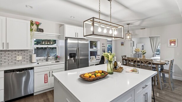 A modern kitchen with white cabinetry, stainless steel appliances, and a central island with fruit. - Hot Tub, Firepit, Deck | 10mins to Beach | Middle Terrace Cottage by AvantStay (Fort Lauderdale)