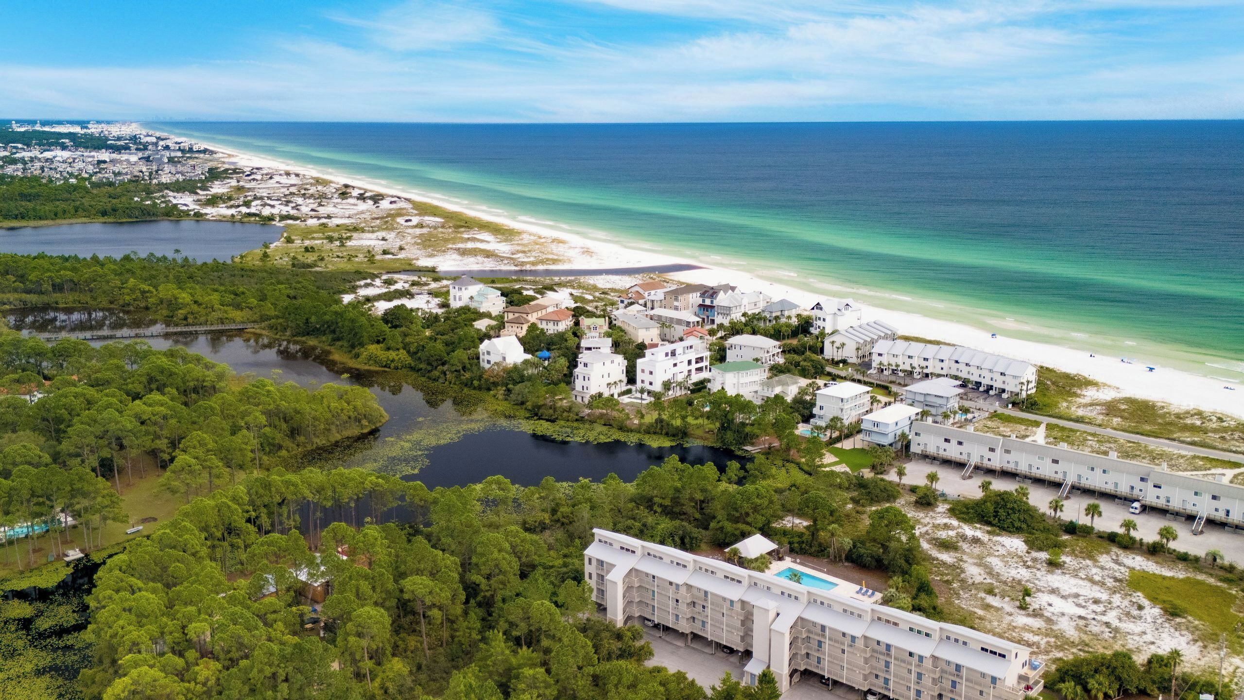An aerial view of a coastal resort with multiple buildings, a beach, and a lake.