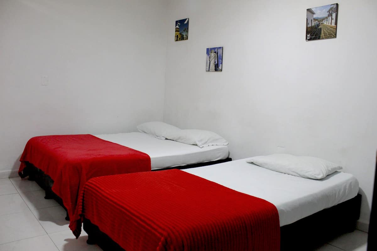 Duas camas de solteiro com colchas vermelhas em um quarto com paredes brancas e piso de azulejos.