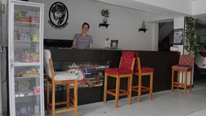 A reception area with a counter, a woman behind it, and a refrigerator stocked with snacks. - Hotel los magueyes  (Bucaramanga)