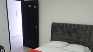 A bedroom with a bed, a red blanket, a dark headboard, and a door with a lock. - Hotel los magueyes  (Bucaramanga)