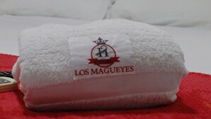 A neatly folded white towel with a logo and text on it, placed on a red towel on a bed. - Hotel los magueyes  (Bucaramanga)