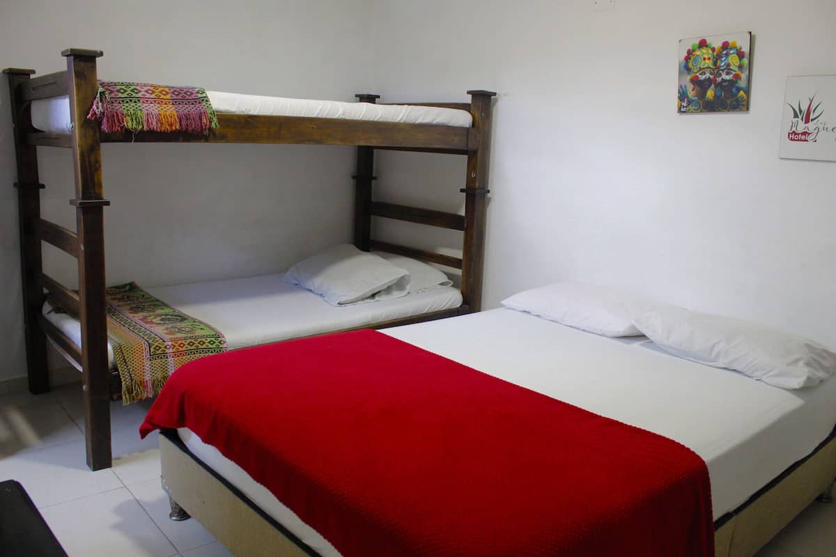 Um quarto com duas beliches, uma com um cobertor vermelho e outra com roupa de cama branca.