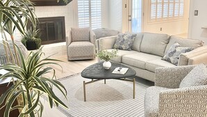 A living room with a sofa, armchairs, a coffee table, a fireplace, and a ceiling fan. - 3 mi to Kyle Field, Farm house Ranchette, sleeps 20! (College Station)