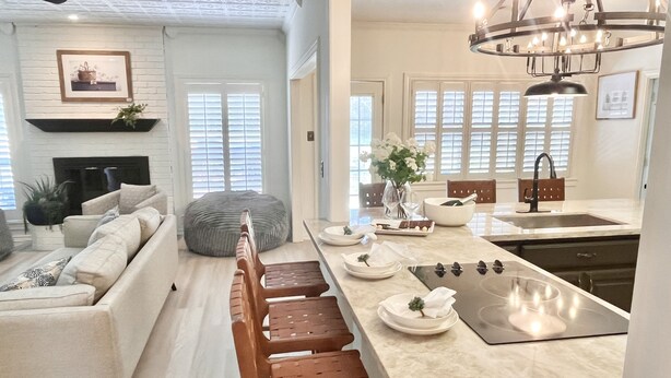 A modern kitchen with a central island, a dining area with a bench, and a living room with a sofa and a fireplace. - 3 mi to Kyle Field, Farm house Ranchette, sleeps 20! (College Station)